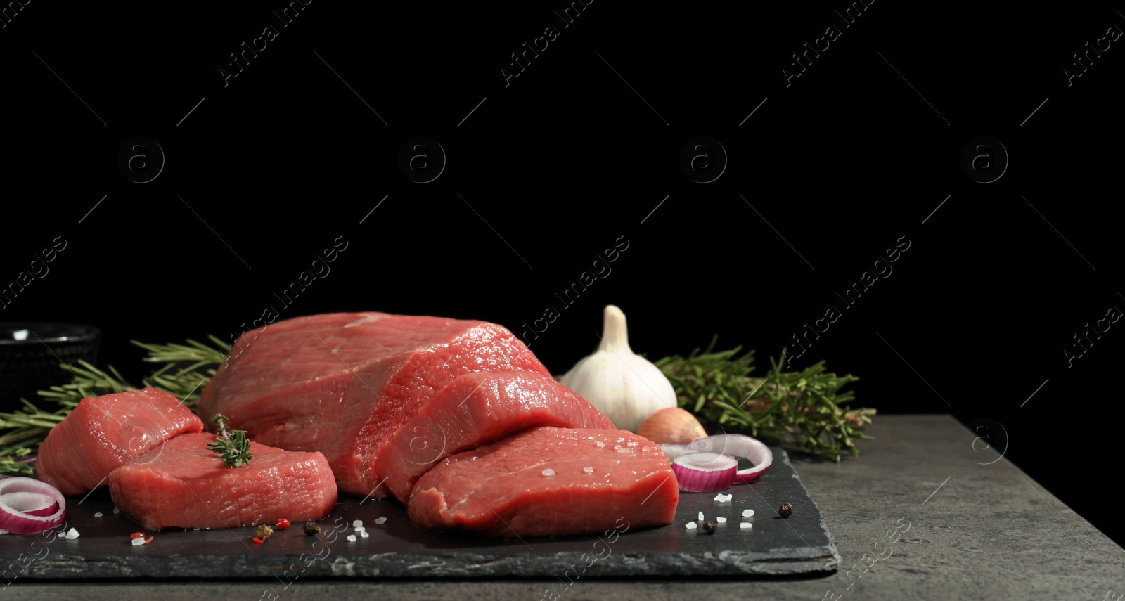 Photo of Slate plate with fresh raw meat on table against dark background