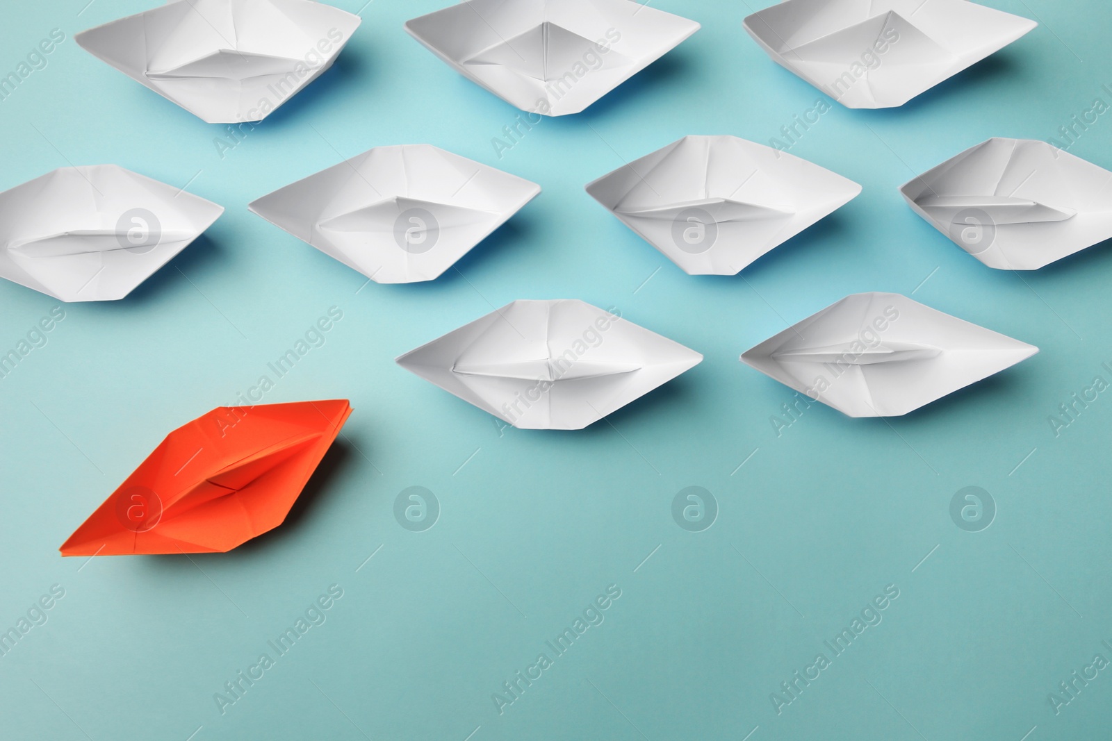 Photo of Orange paper boat floating away from others on light background, flat lay. Uniqueness concept