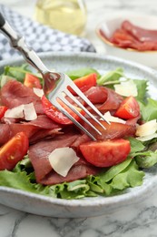 Eating delicious bresaola salad with tomatoes and parmesan cheese on white marble table, closeup