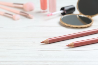 Photo of Lip pencils and other makeup products on white wooden table, space for text