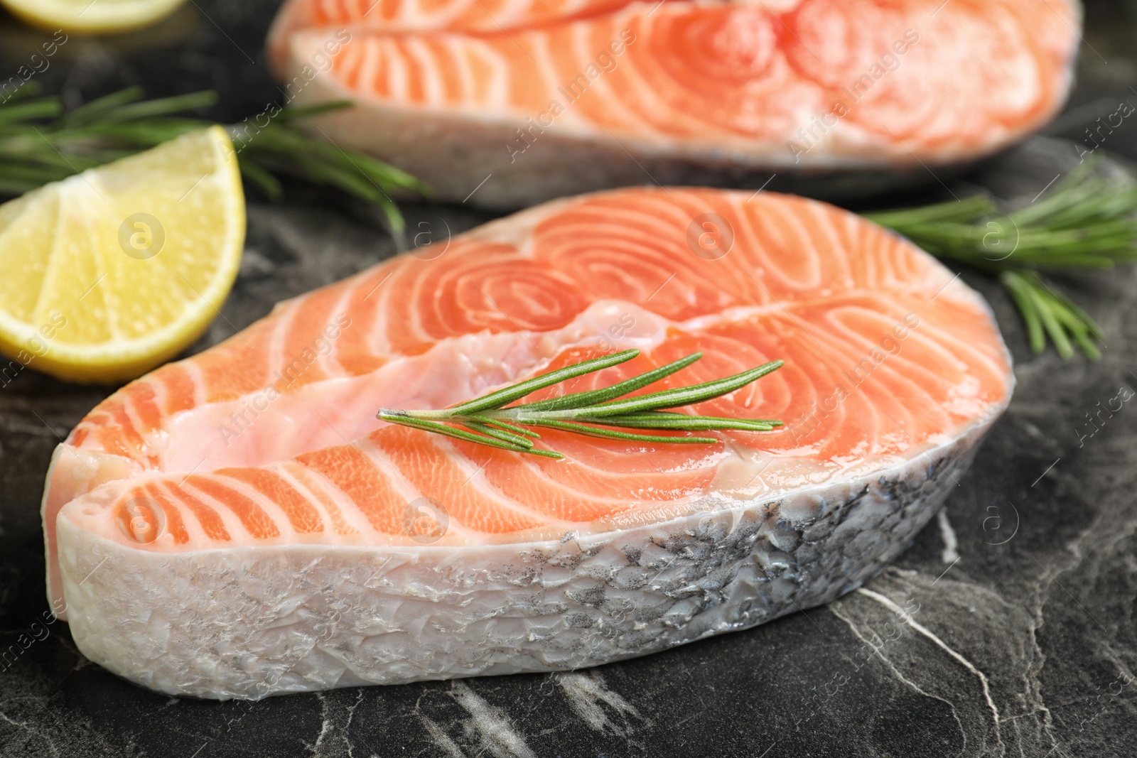 Photo of Fresh raw salmon, rosemary and lemon on black marble table. Fish delicacy