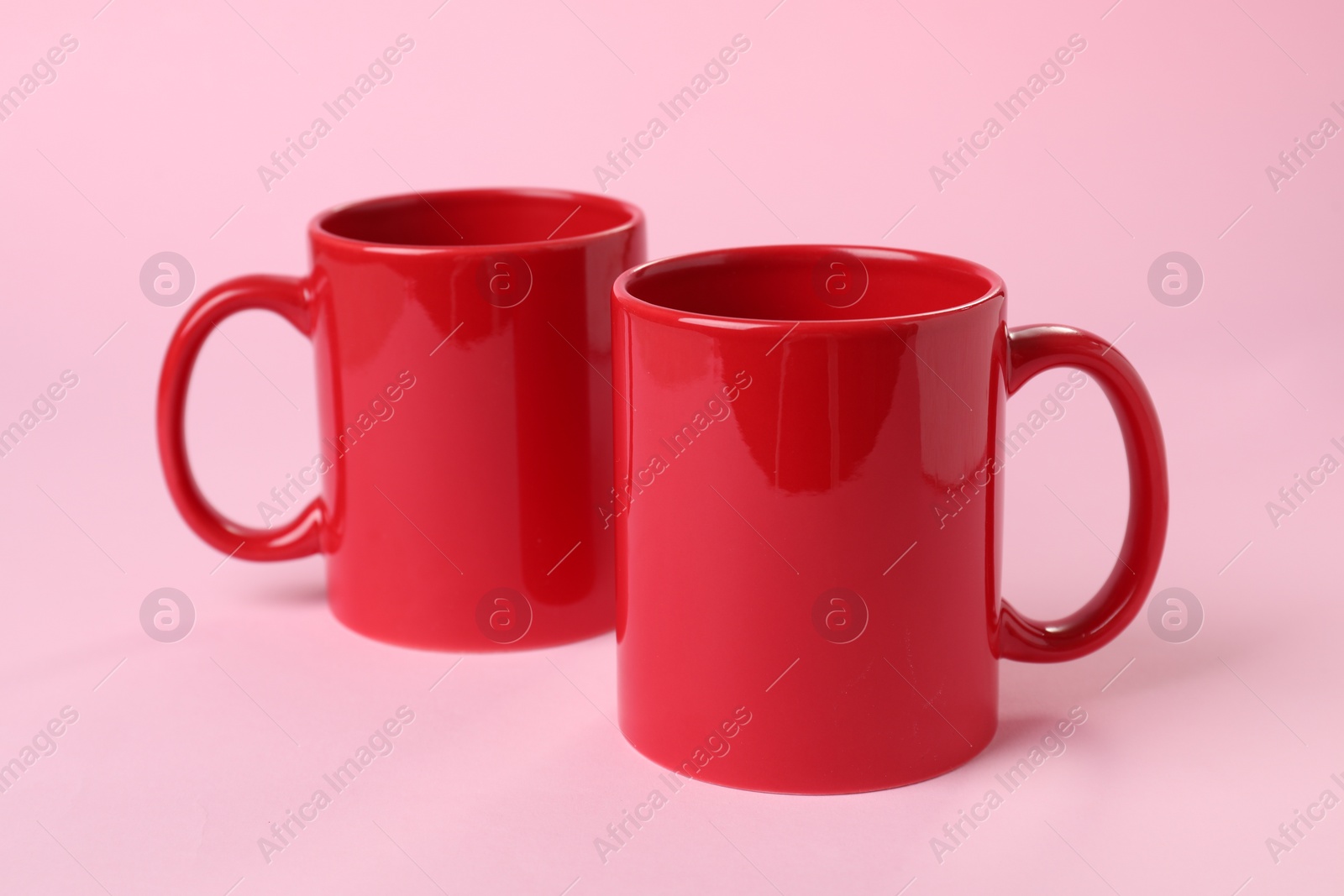 Photo of Two red ceramic mugs on pink background