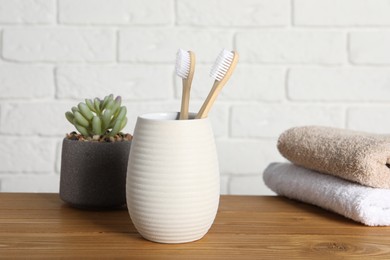 Photo of Bamboo toothbrushes in holder, houseplant and towels on wooden table