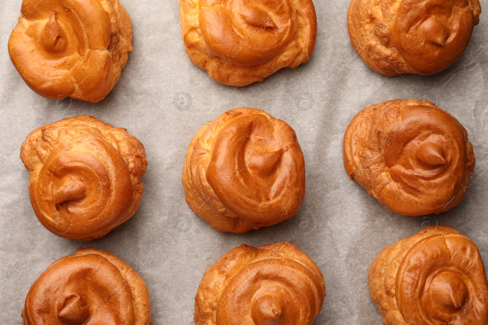 Photo of Delicious profiteroles on parchment paper, flat lay