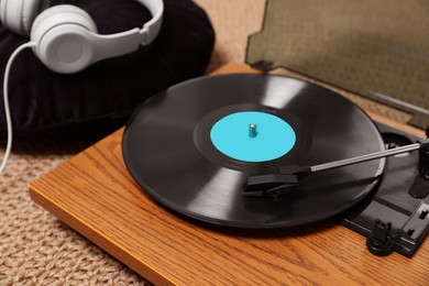 Photo of Stylish turntable with vinyl disc and headphones on carpet at home, closeup