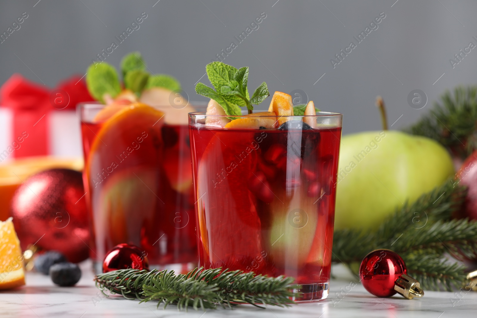 Photo of Aromatic Sangria drink in glasses, ingredients and Christmas decor on white marble table