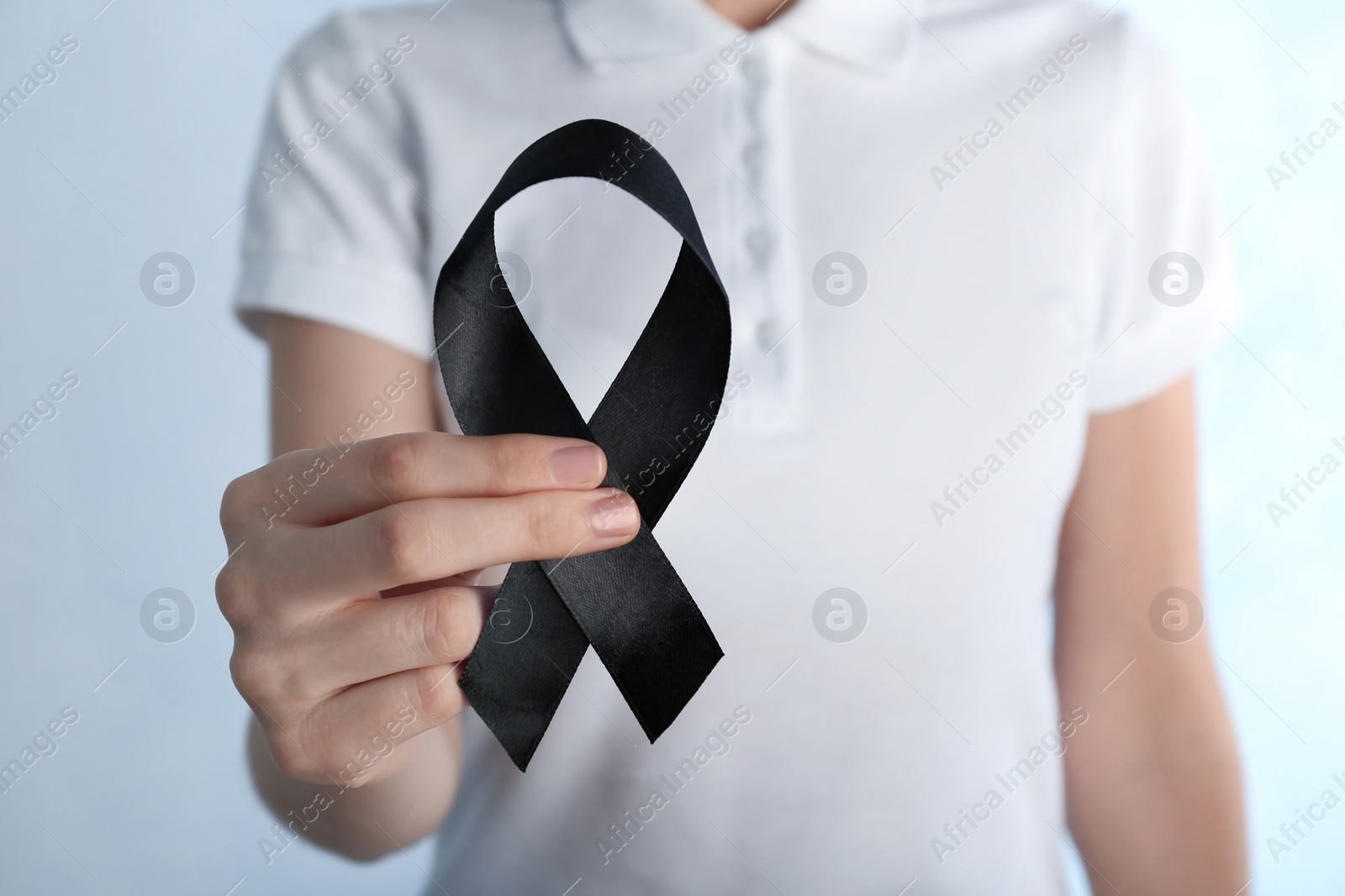 Photo of Woman holding black ribbon on light background, closeup. Funeral symbol