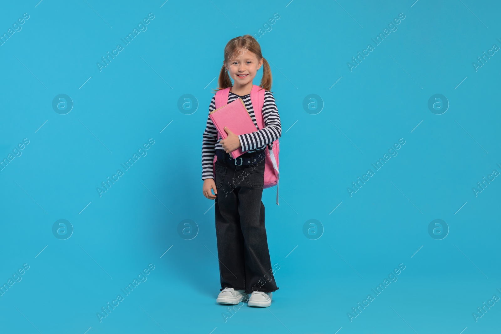 Photo of Happy schoolgirl with backpack and books on light blue background