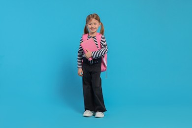 Happy schoolgirl with backpack and books on light blue background