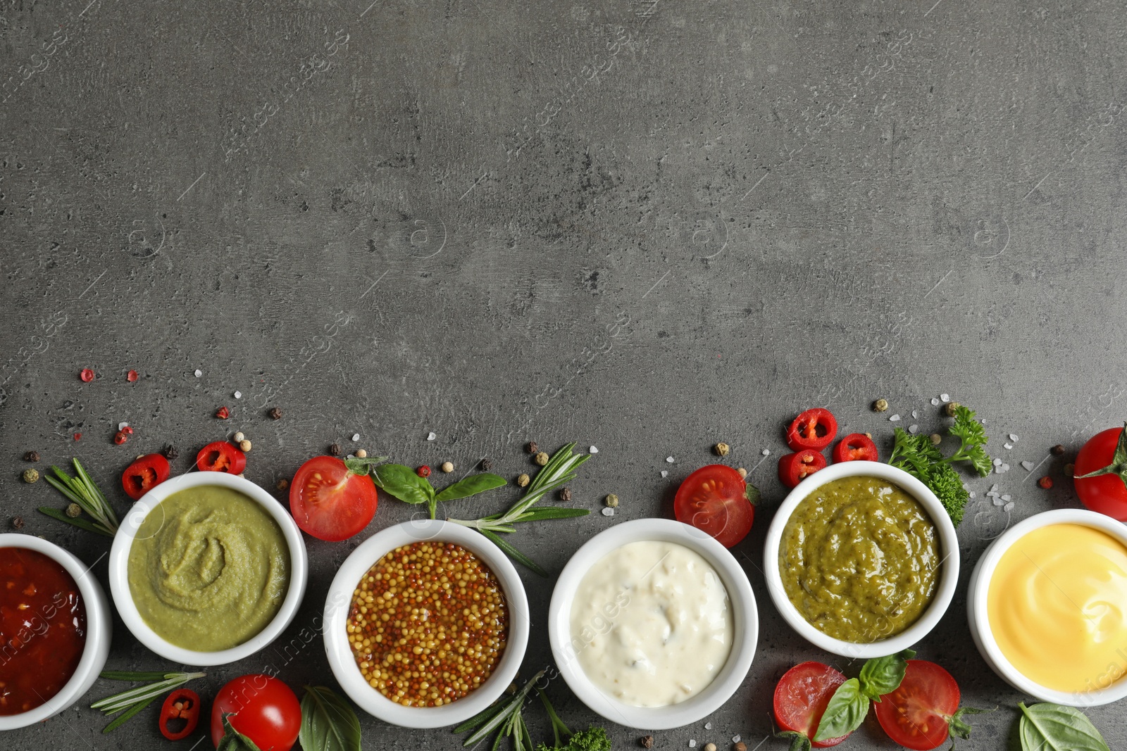 Photo of Bowls with different sauces and ingredients on gray background, flat lay. Space for text