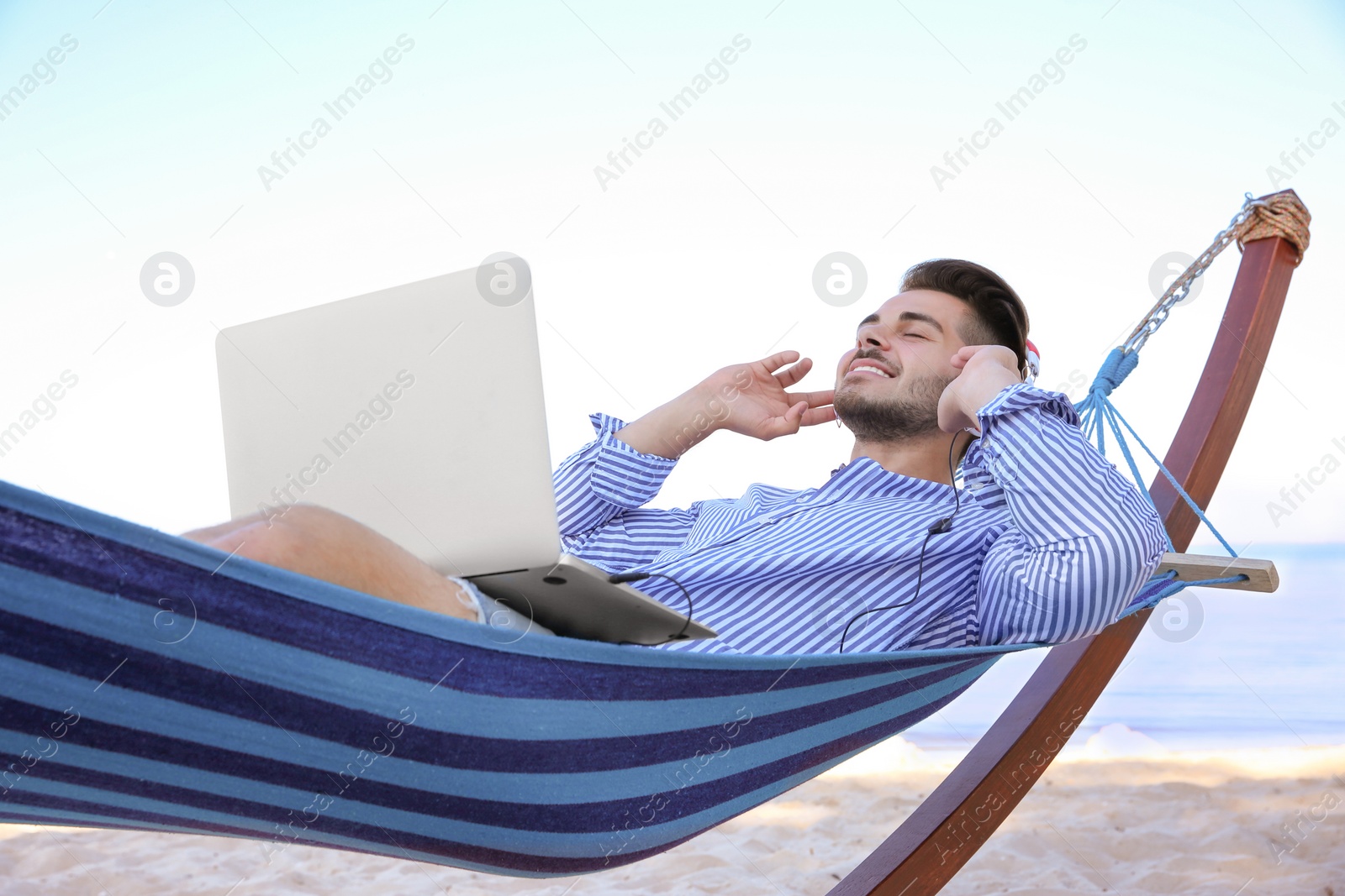 Photo of Young man listening to music in comfortable hammock at seaside