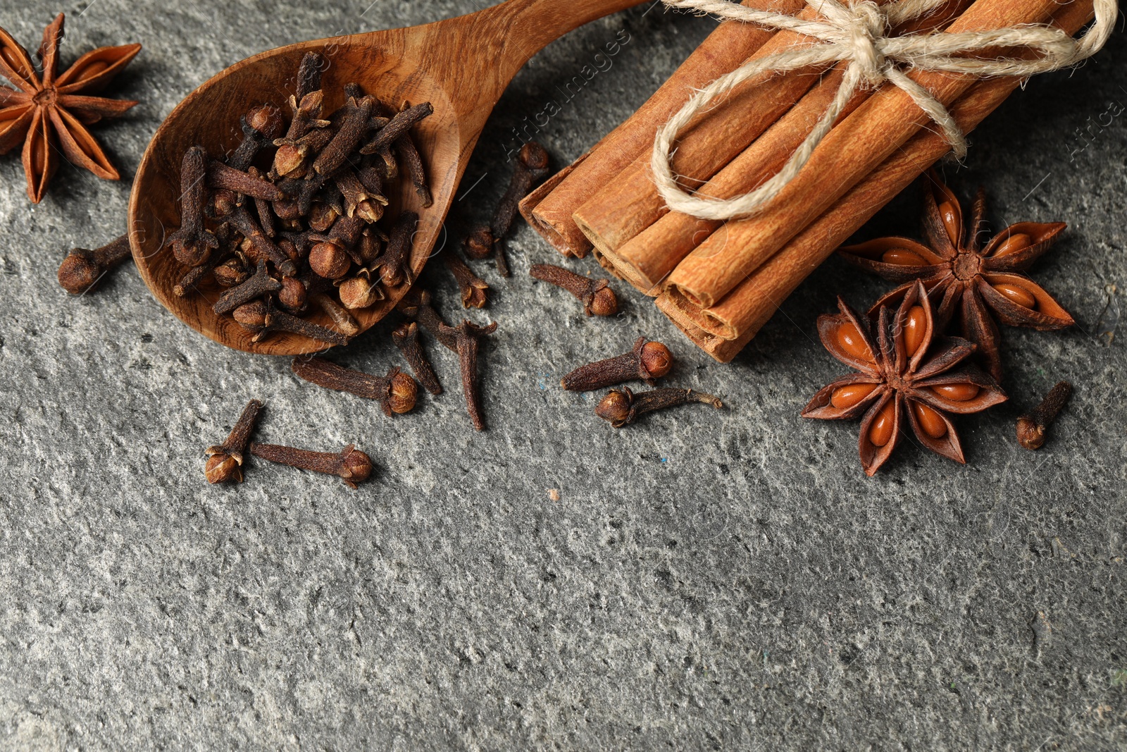 Photo of Wooden spoon with different spices on gray textured table, flat lay. Space for text