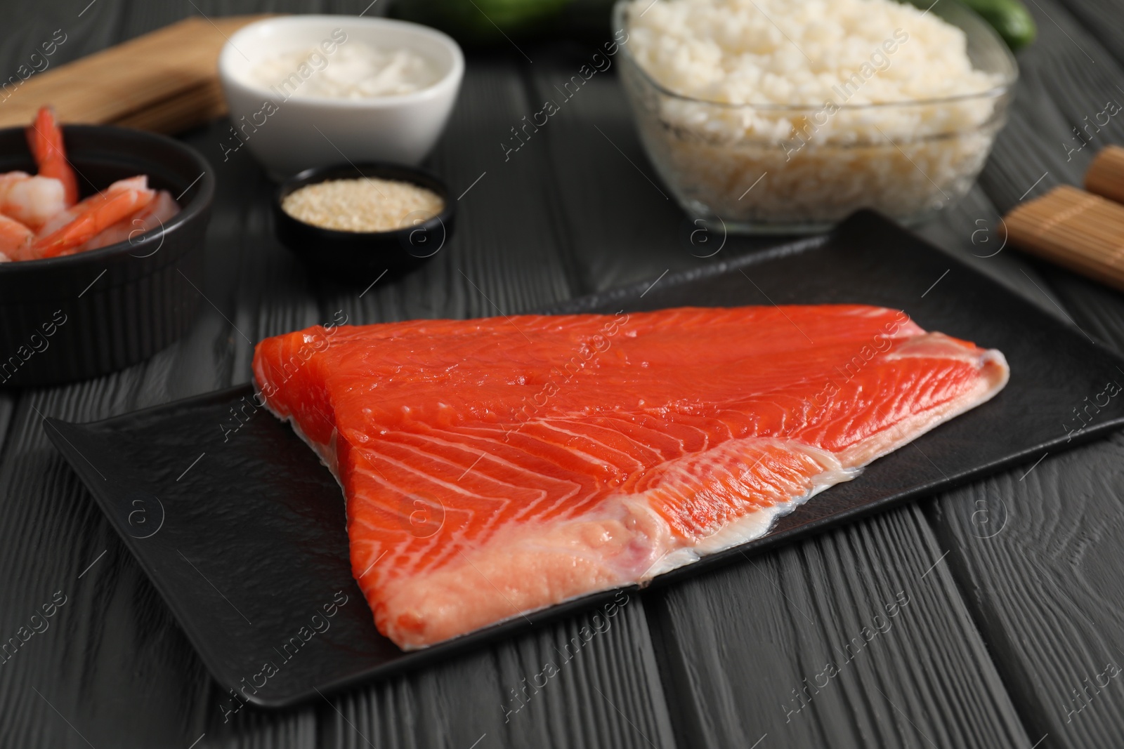 Photo of Making sushi rolls. Fresh salmon and other ingredients on black wooden table, closeup