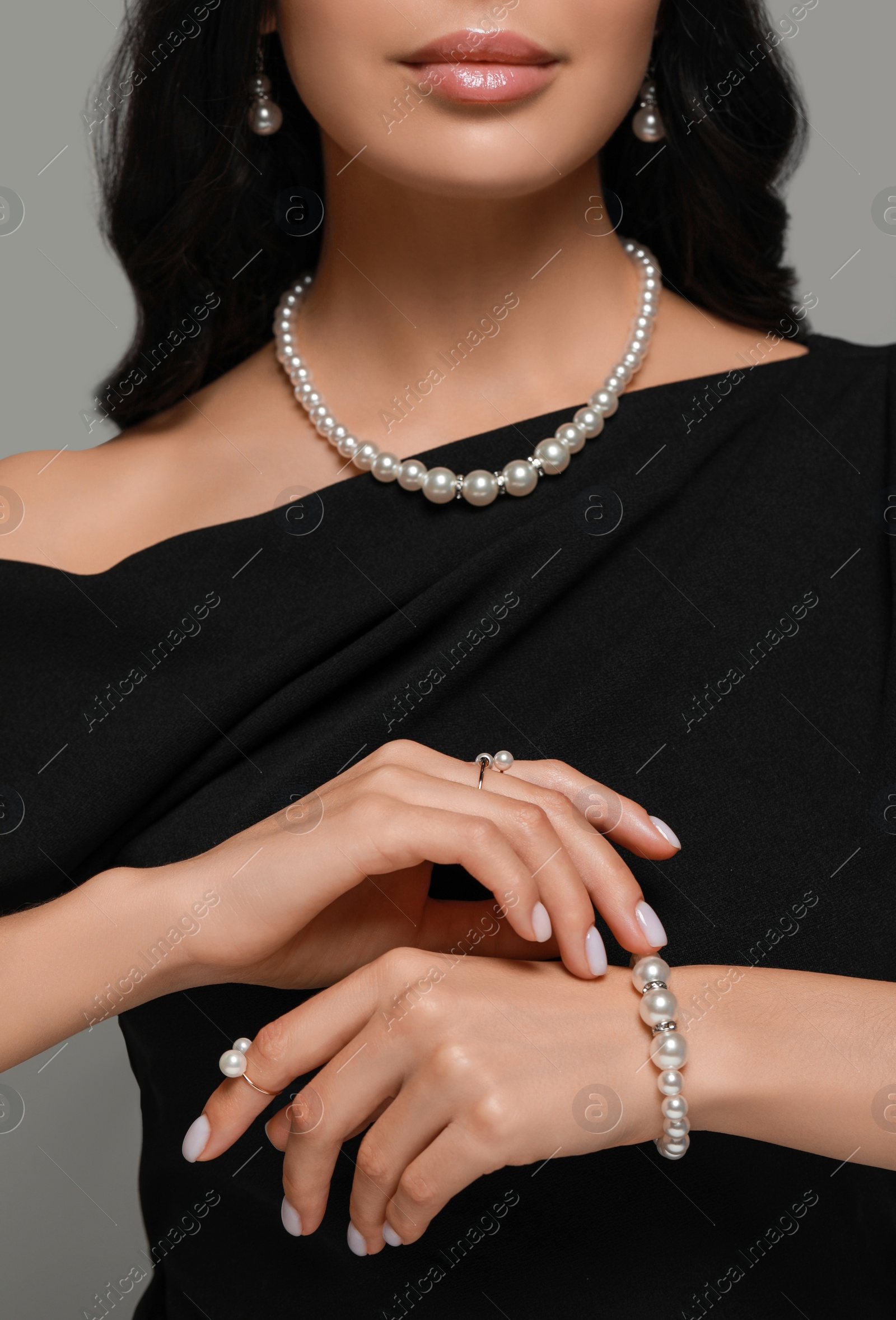 Photo of Young woman wearing elegant pearl jewelry on grey background, closeup