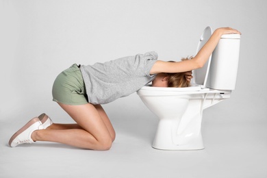 Photo of Young woman vomiting in toilet bowl on gray background