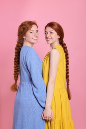 Photo of Portrait of beautiful young redhead sisters with braided hair on pink background
