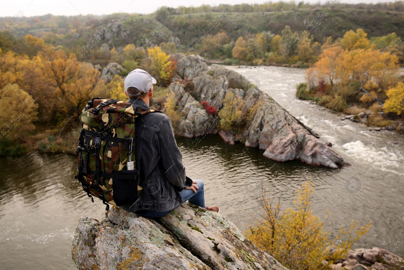 Photo of Hiker with travel backpack sitting on steep cliff near mountain river