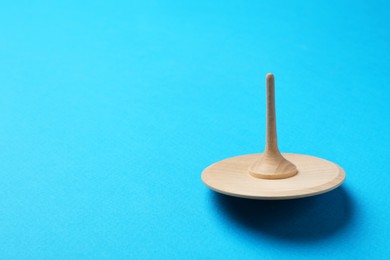 Photo of One wooden spinning top on light blue background, space for text