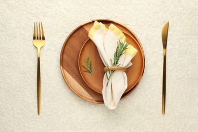 Photo of Stylish setting with cutlery, napkin, rosemary and plates on light textured table, flat lay