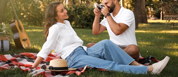 Image of Man taking picture of his girlfriend on picnic plaid in summer park. Banner design