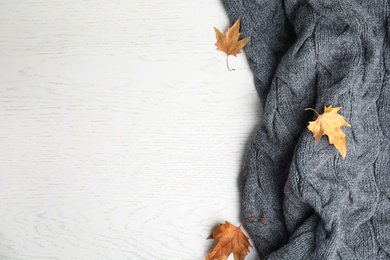 Photo of Knitted plaid and dry leaves on white wooden table, flat lay. Space for text