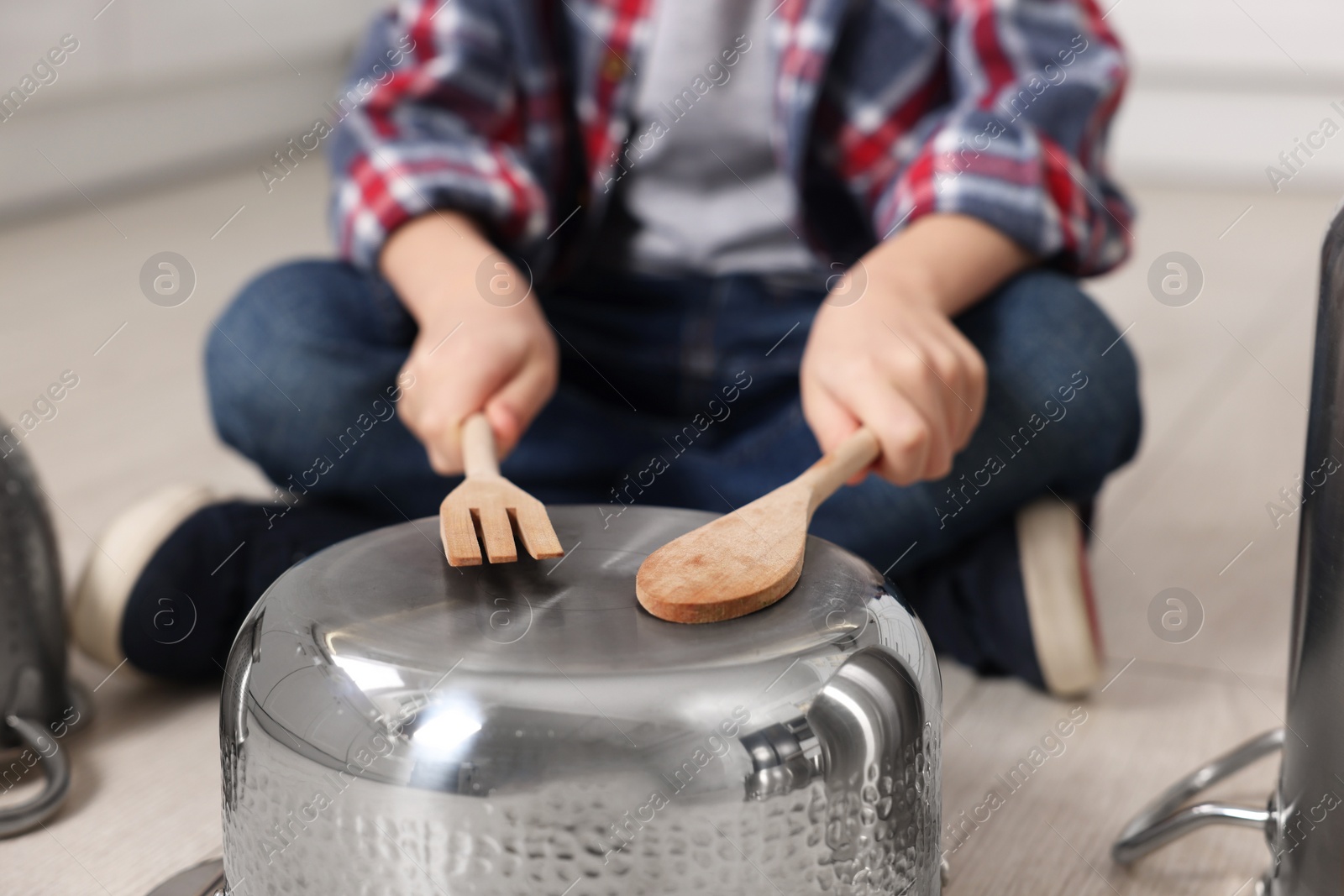 Photo of Little boy pretending to play drum on pot indoors, closeup