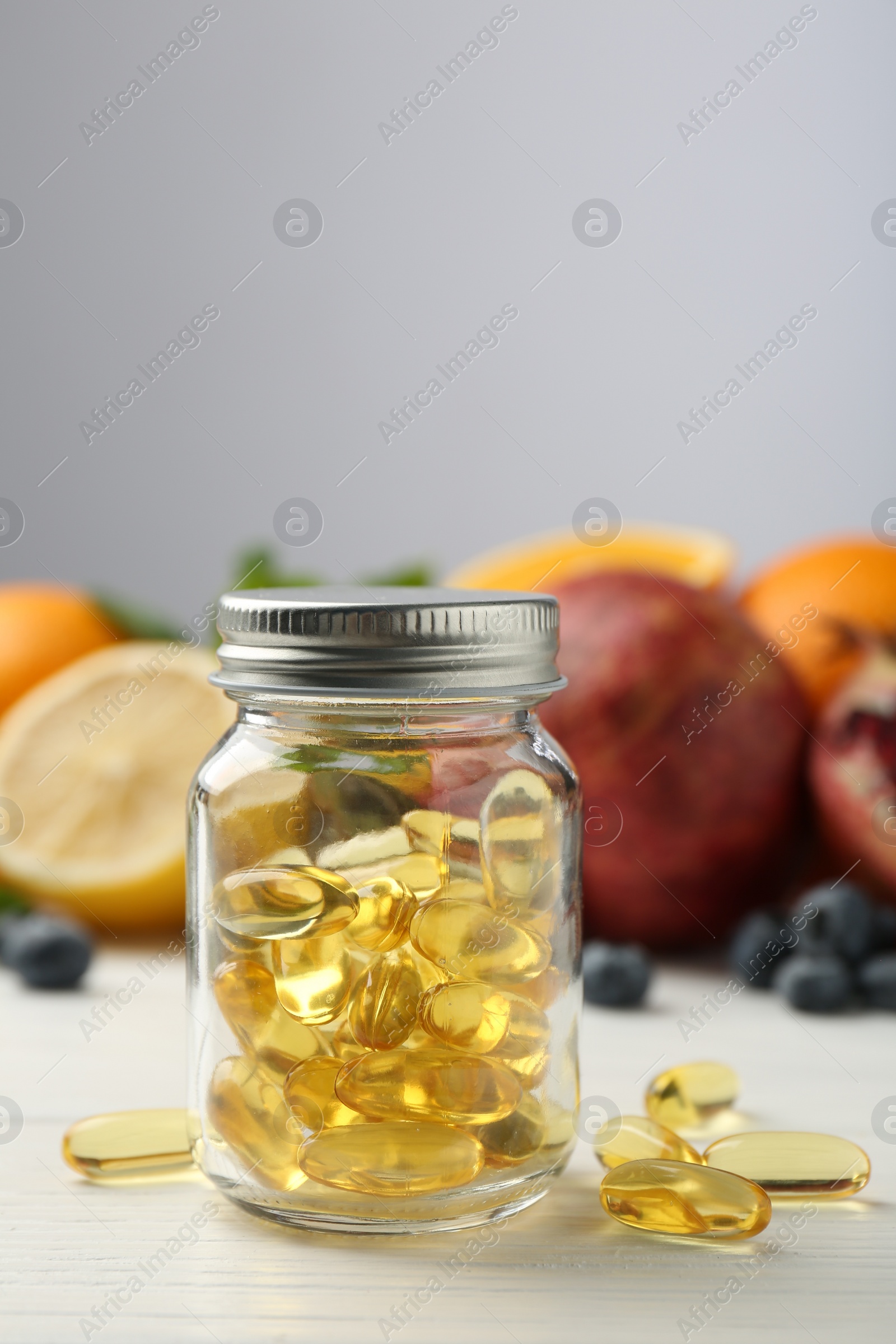 Photo of Vitamin pills in bottle and fresh fruits on white wooden table