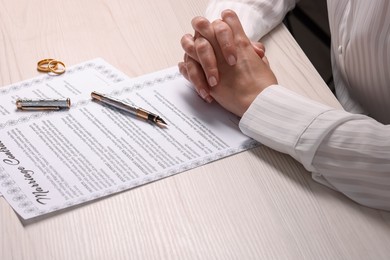 Photo of Woman signing marriage contract at light wooden table, closeup