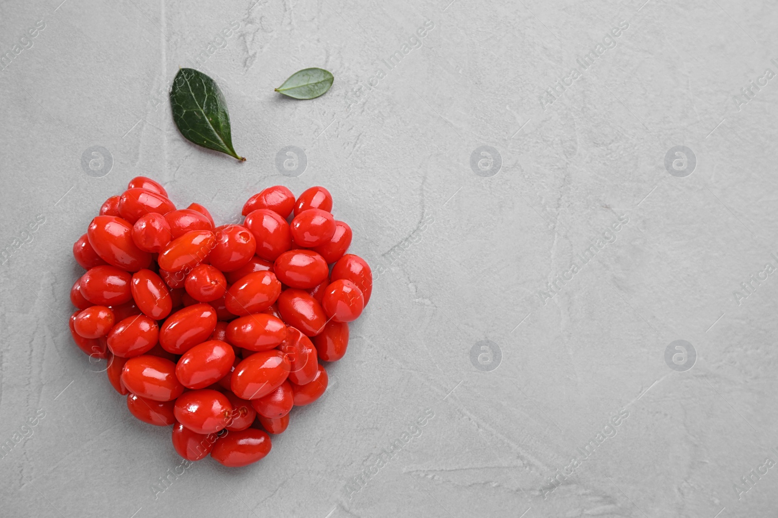 Photo of Heart made of fresh goji berries and leaves on grey background, flat lay. Space for text