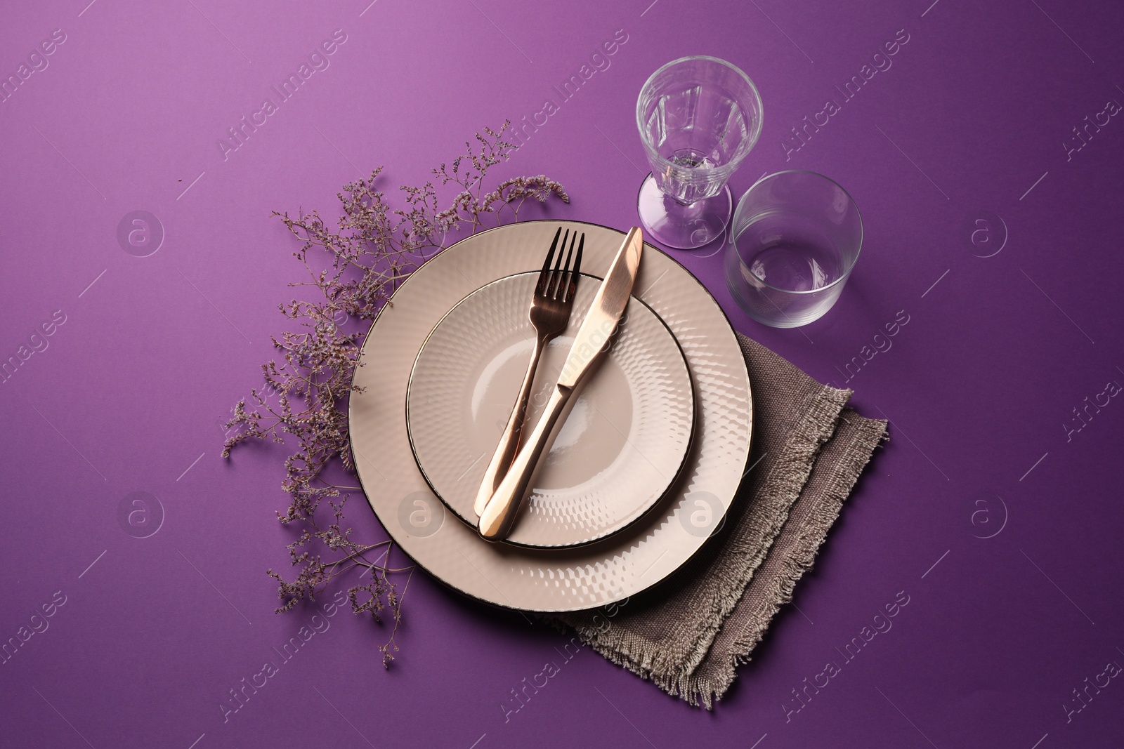 Photo of Stylish table setting. Plates, cutlery, glasses and floral decor on purple background, flat lay