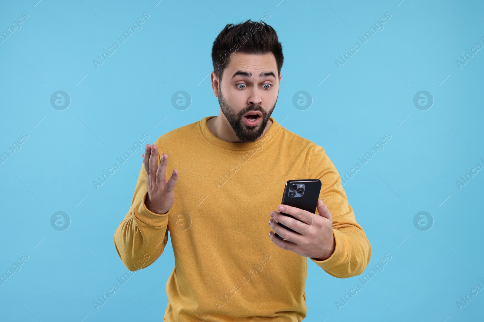 Photo of Shocked young man using smartphone on light blue background