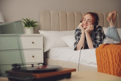 Photo of Young woman listening to music with turntable in bedroom