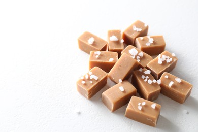 Tasty caramel candies and salt on white table, space for text