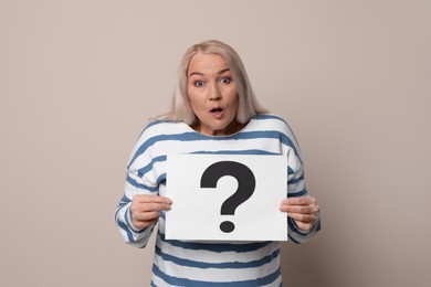Photo of Emotional mature woman holding paper with question mark on beige background