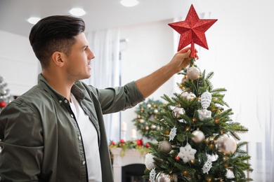 Man decorating Christmas tree with star topper indoors