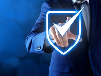 Anti-fraud security system. Man pointing at illustration of checkmark in shield on blue background, closeup. Space for text