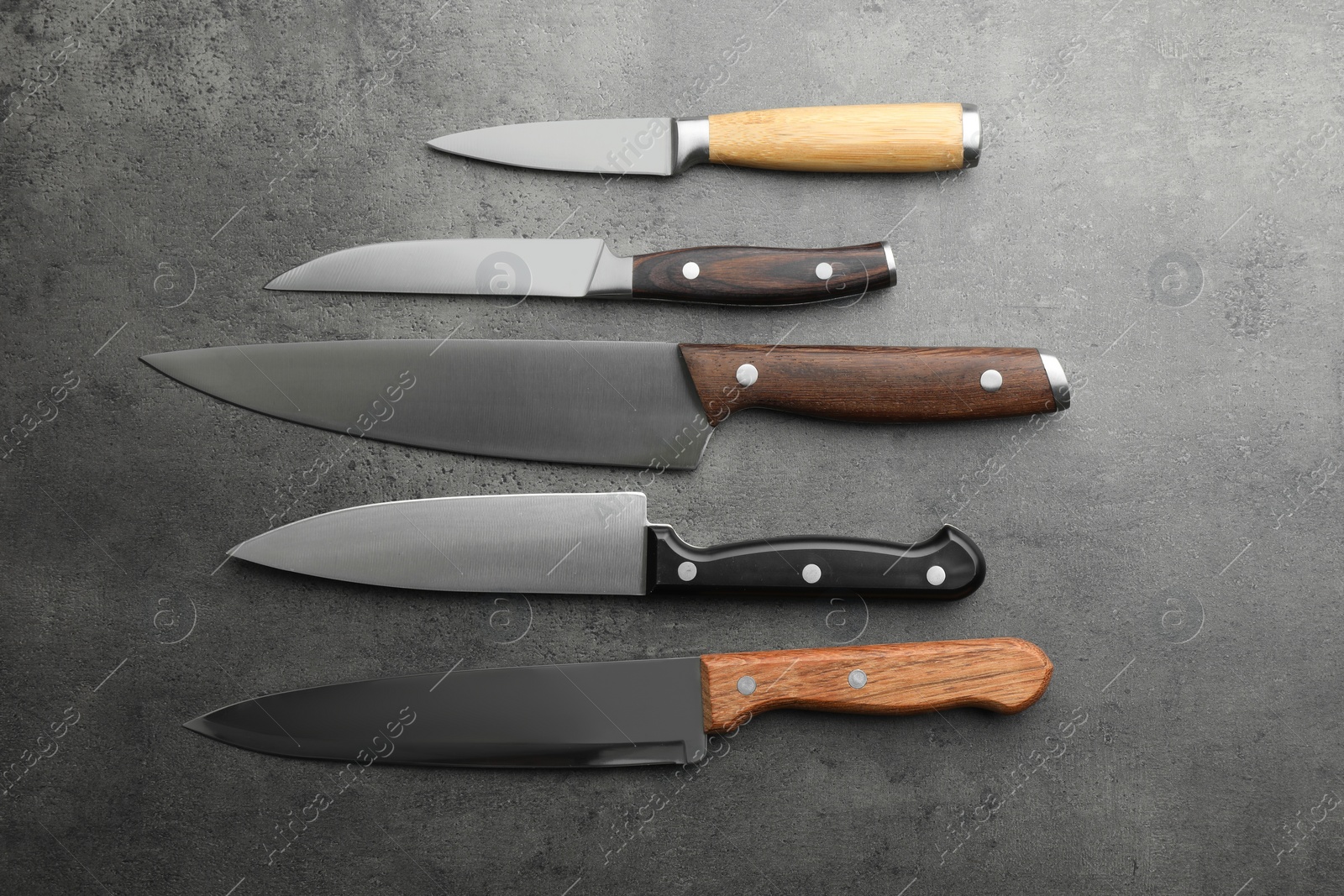 Photo of Many different knives on grey textured table, flat lay