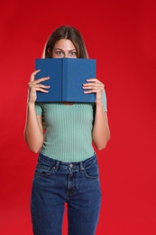 Beautiful young woman with book on red background. Reading time