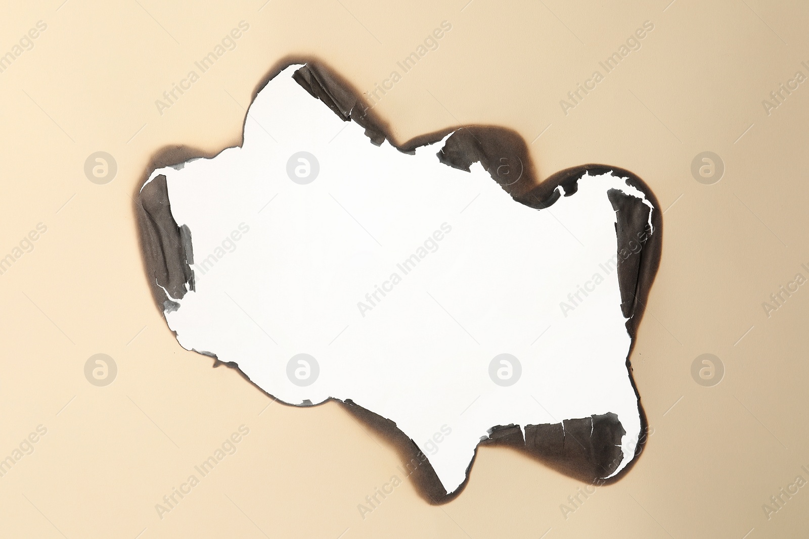 Photo of Burnt hole in beige paper on white background