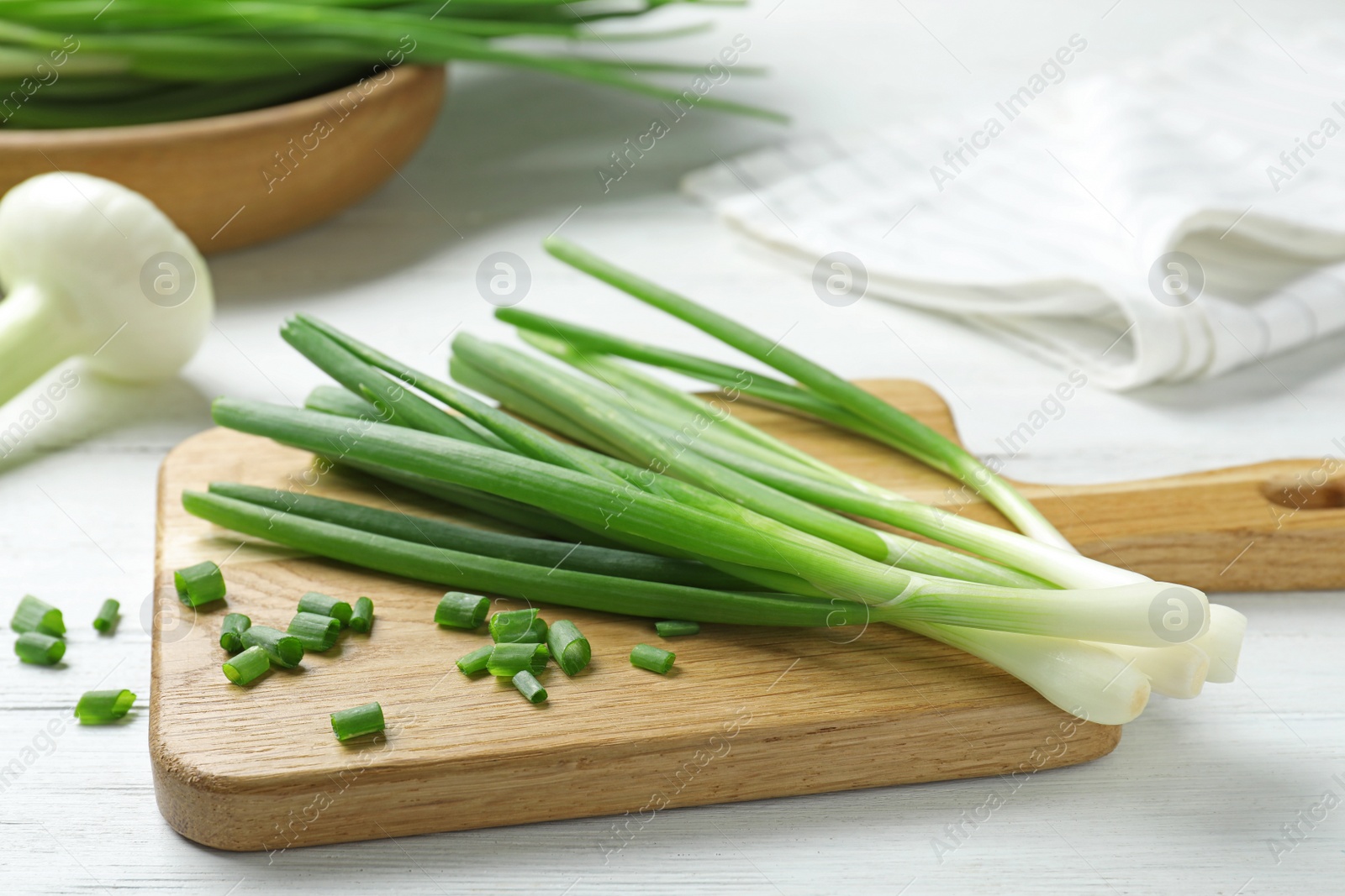 Photo of Wooden board with cut fresh green onions on white table