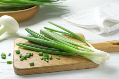 Photo of Wooden board with cut fresh green onions on white table