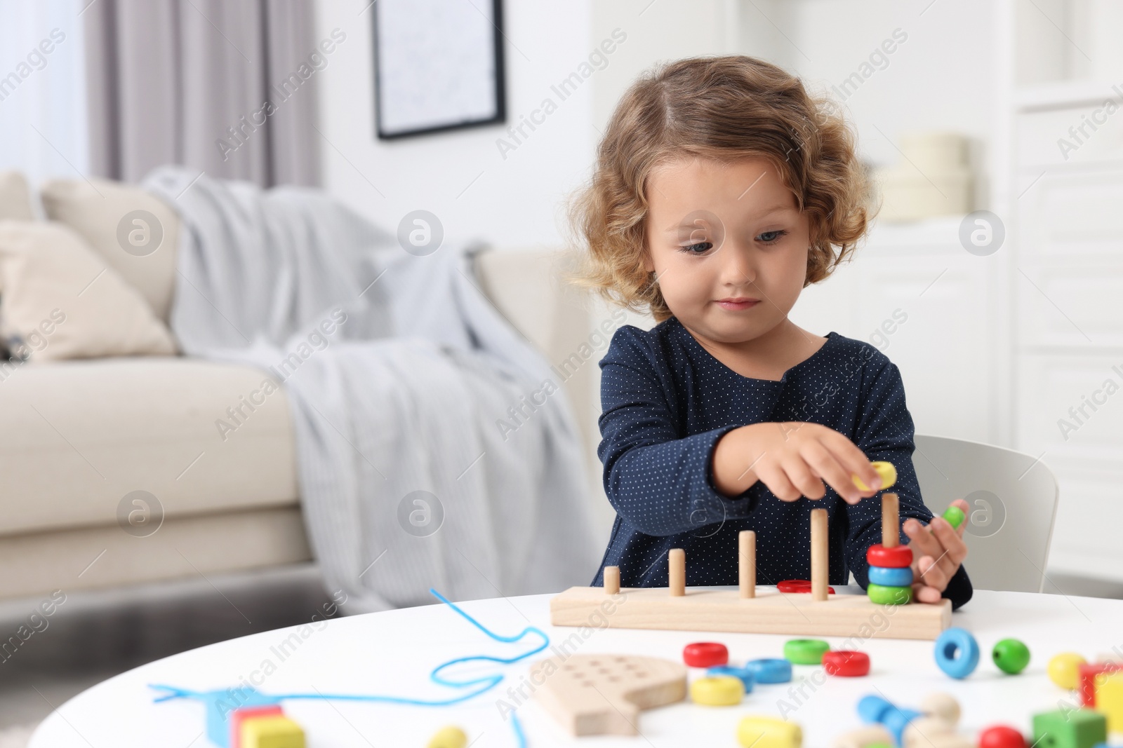 Photo of Motor skills development. Little girl playing with stacking and counting game at table indoors