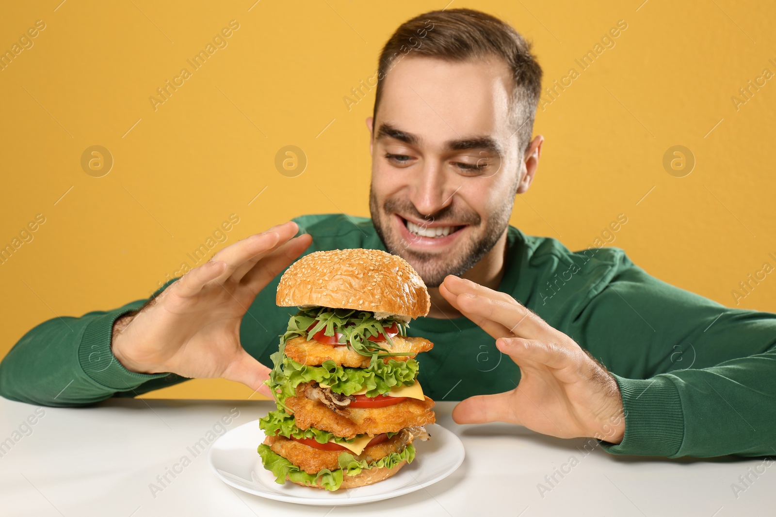 Photo of Young hungry man eating huge burger at table