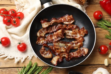 Photo of Delicious bacon slices in frying pan and products on wooden table, flat lay