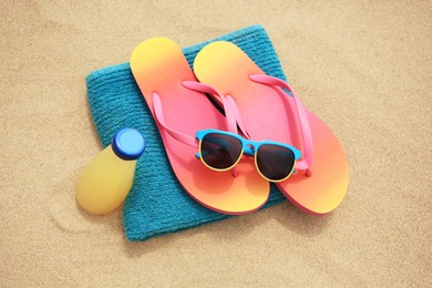 Stylish sunglasses, flip flops. towel and bottle of refreshing drink on sand, above view