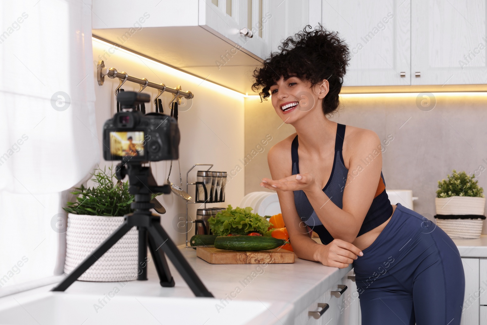 Photo of Smiling food blogger explaining something while recording video in kitchen