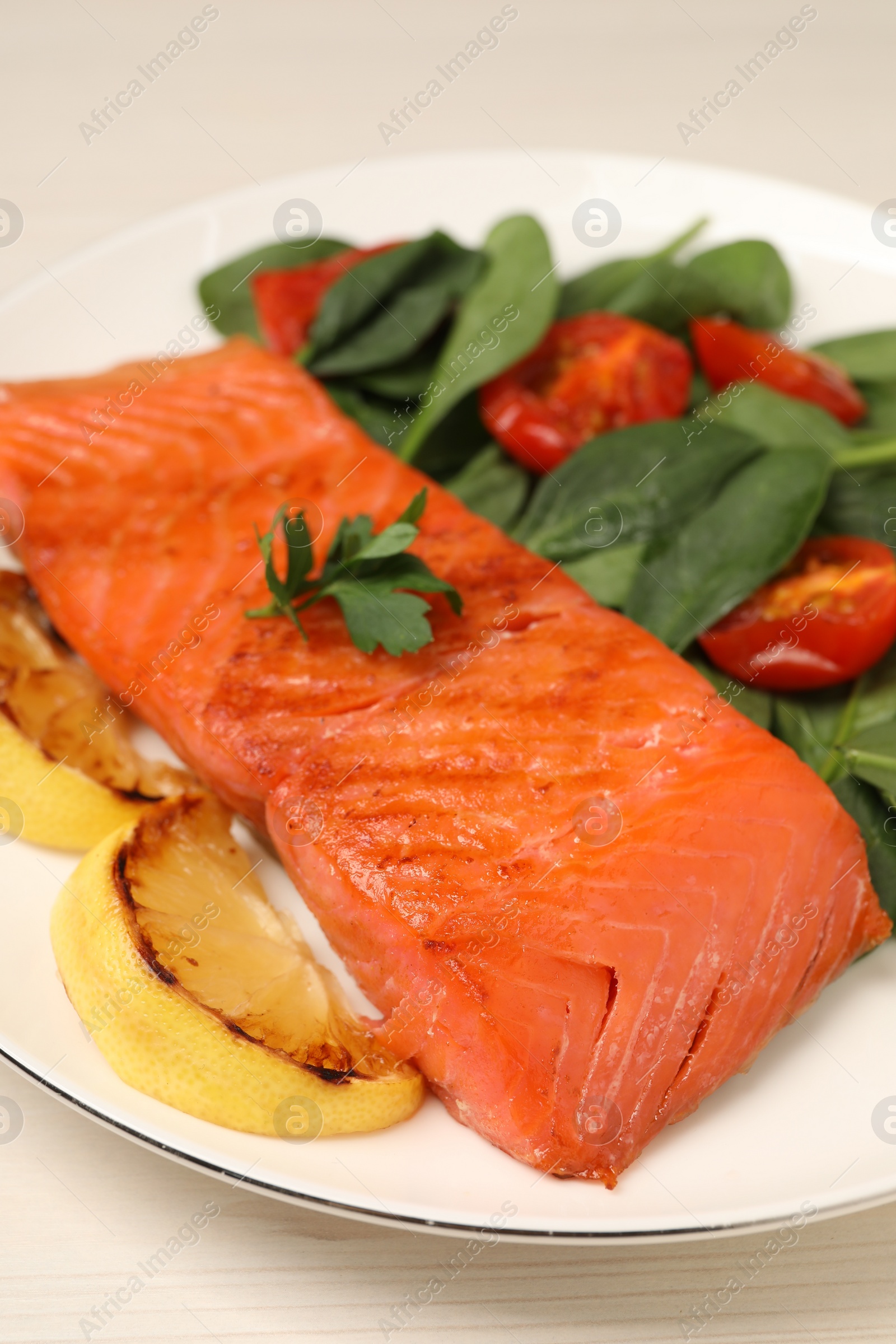 Photo of Tasty grilled salmon with basil, tomatoes and lemon on white wooden table, closeup