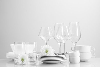 Photo of Set of many clean dishware, cutlery, glasses and flowers on light table