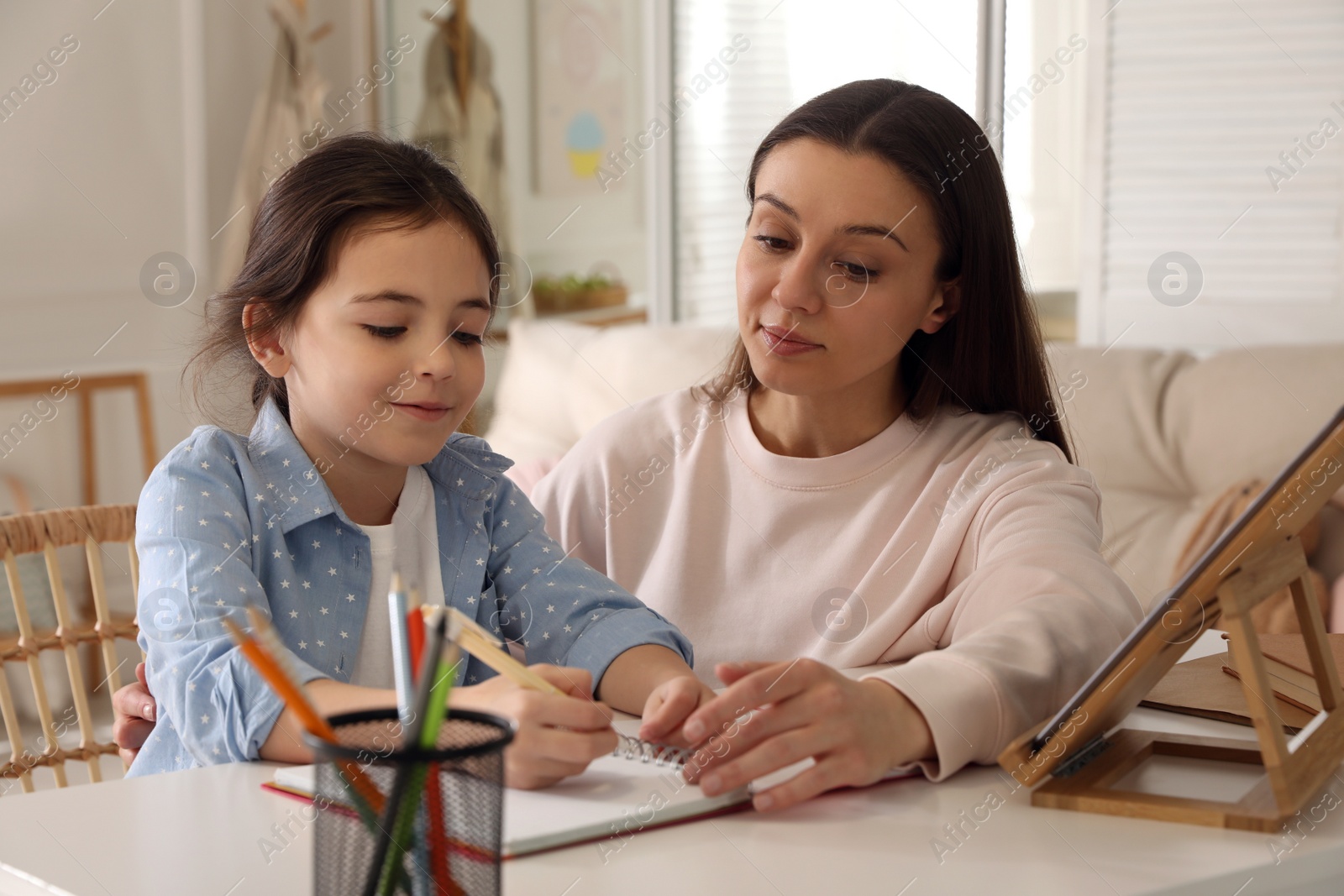 Photo of Mother helping her daughter with homework using tablet at home