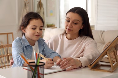 Photo of Mother helping her daughter with homework using tablet at home